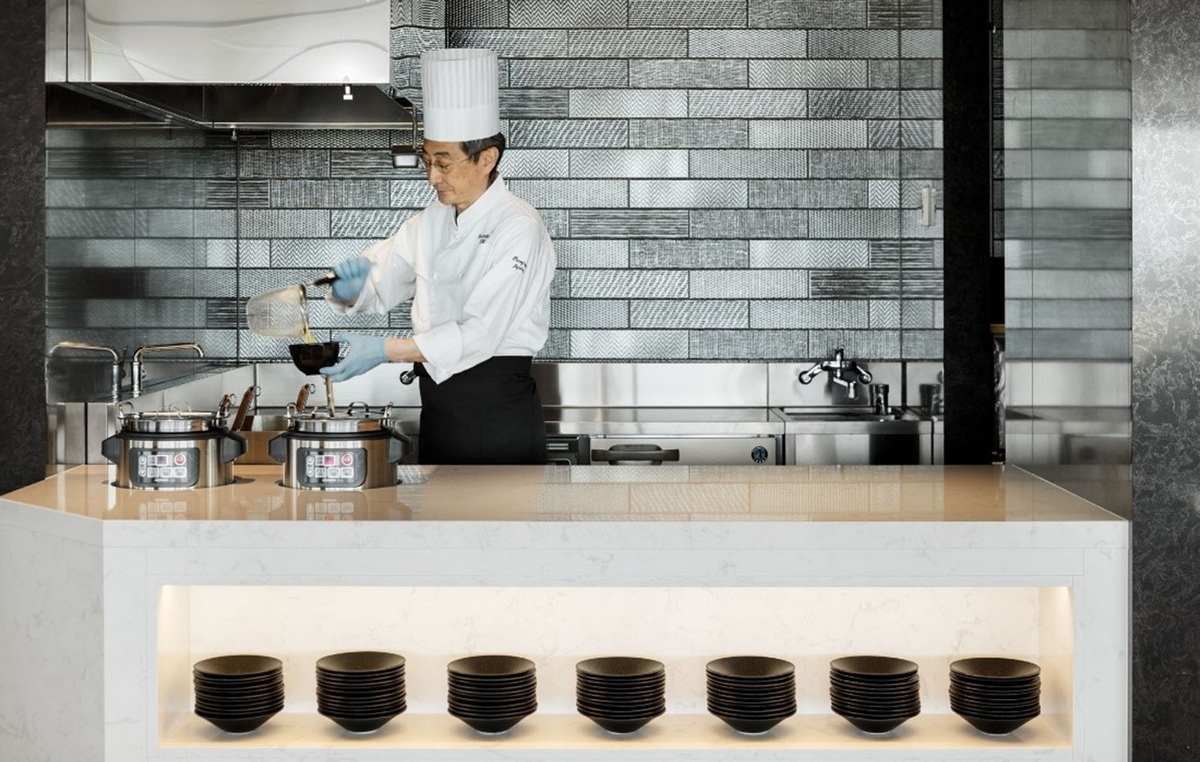 a man with a chef hat, pouring noodles from a bowl.