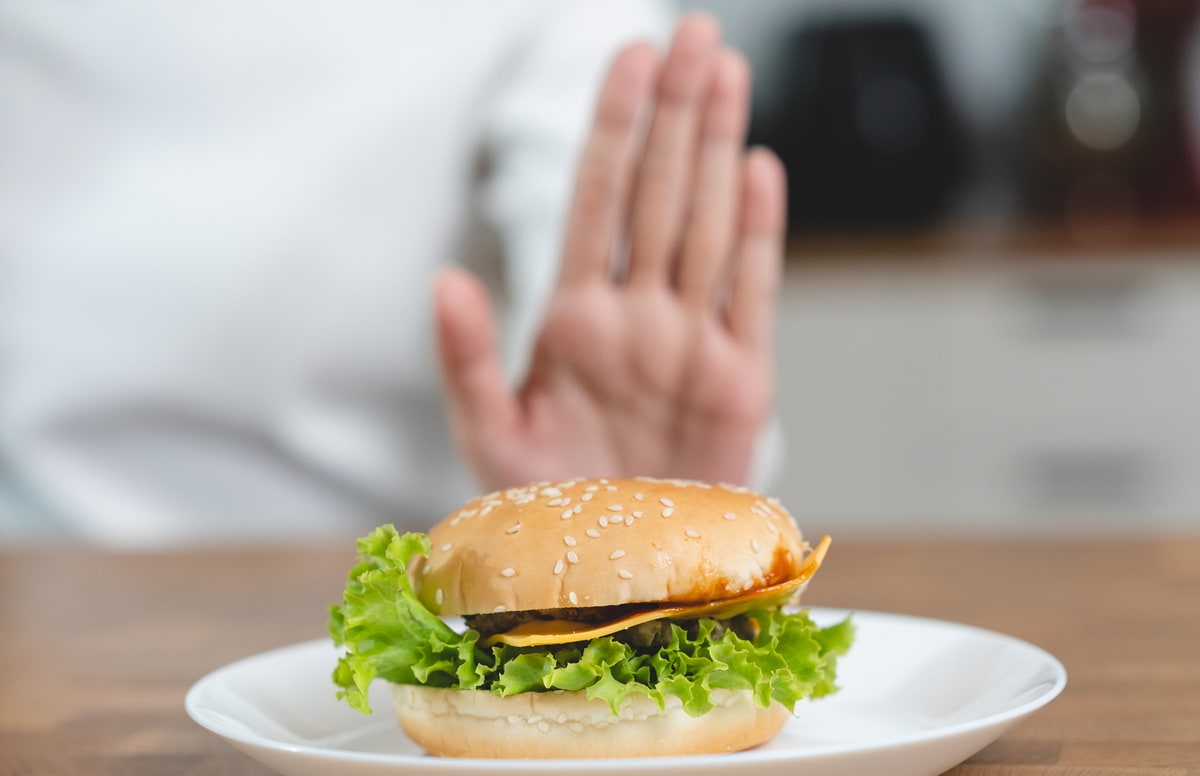 Hamburger on a plate with the palm of a hand showing stop.