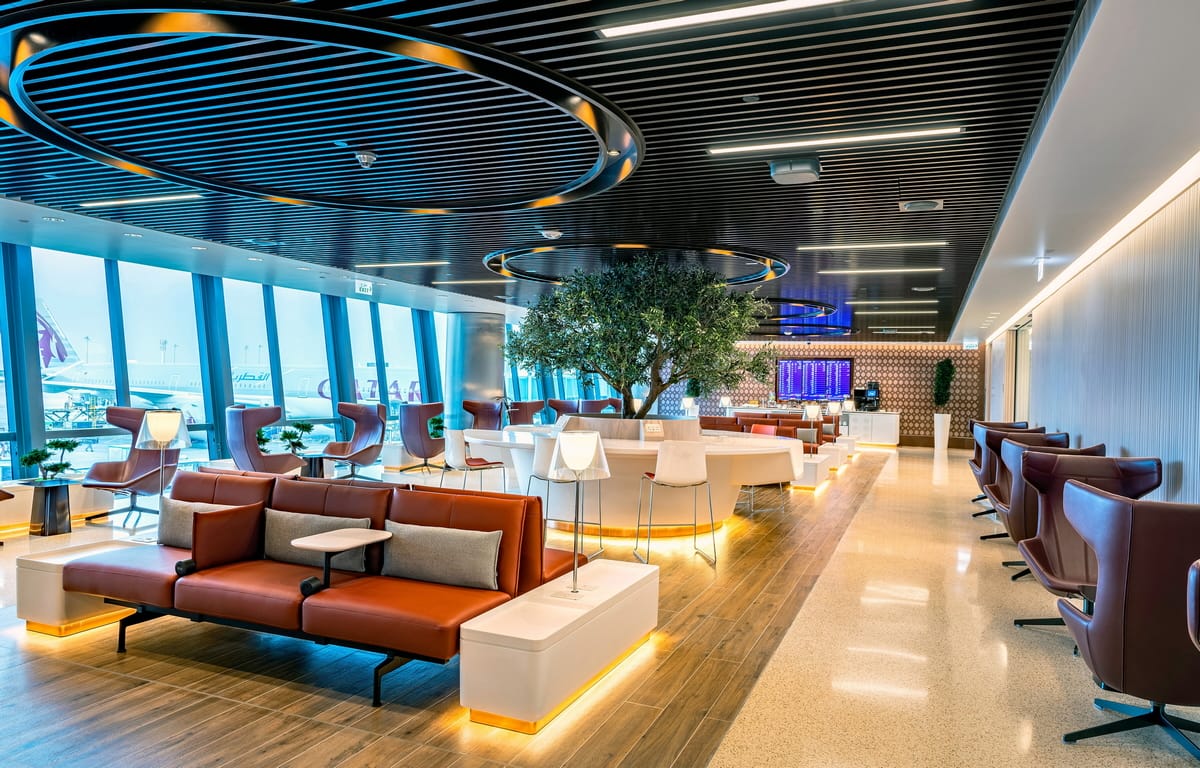 Lounge with chairs and tables, with large windows in the background.
