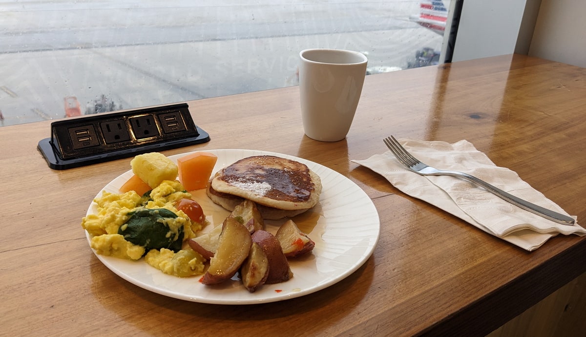plate of breakfast food on wooden table, at a window table with view outside.