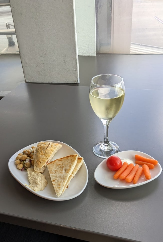 hummus, pita, and veggies with a glass of white wine sitting on a table.