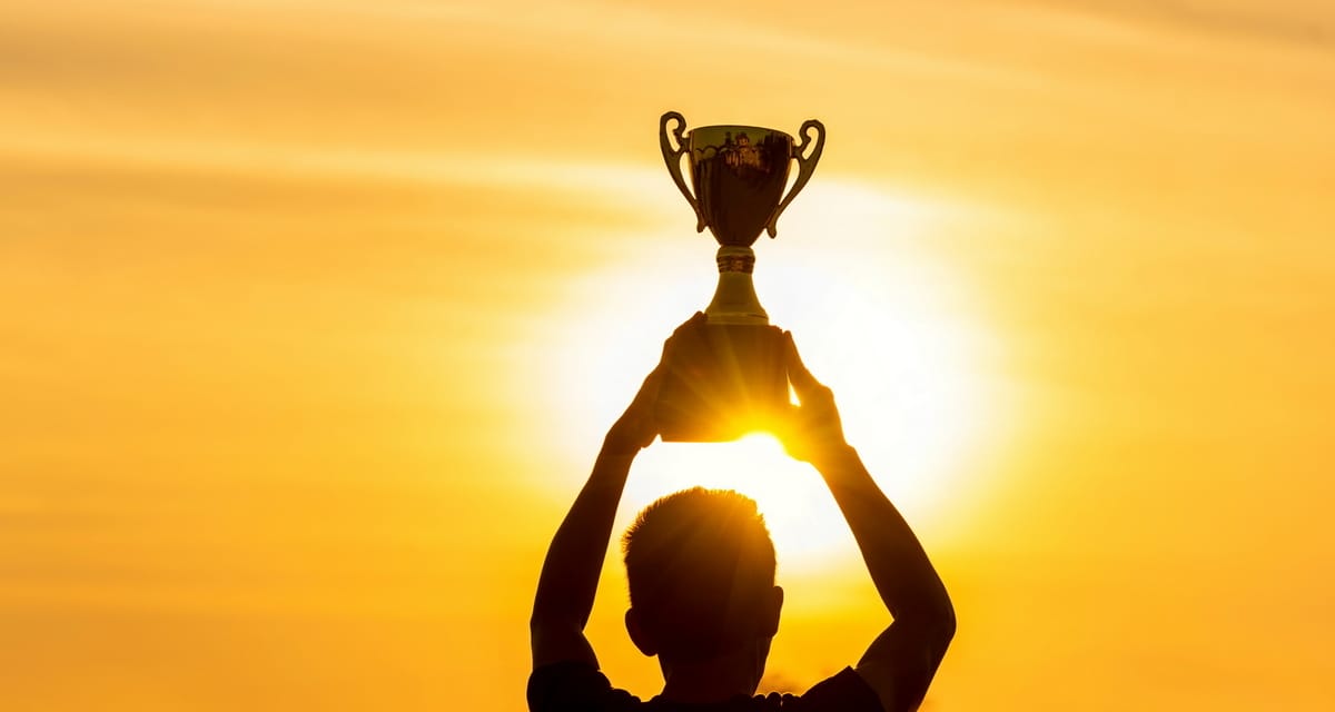 Person holding a trophy up in with the sun setting in background.