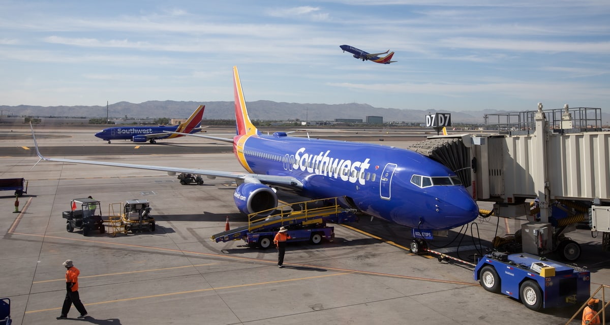 Southwest Airlines plane at gate and plane taking off in background.