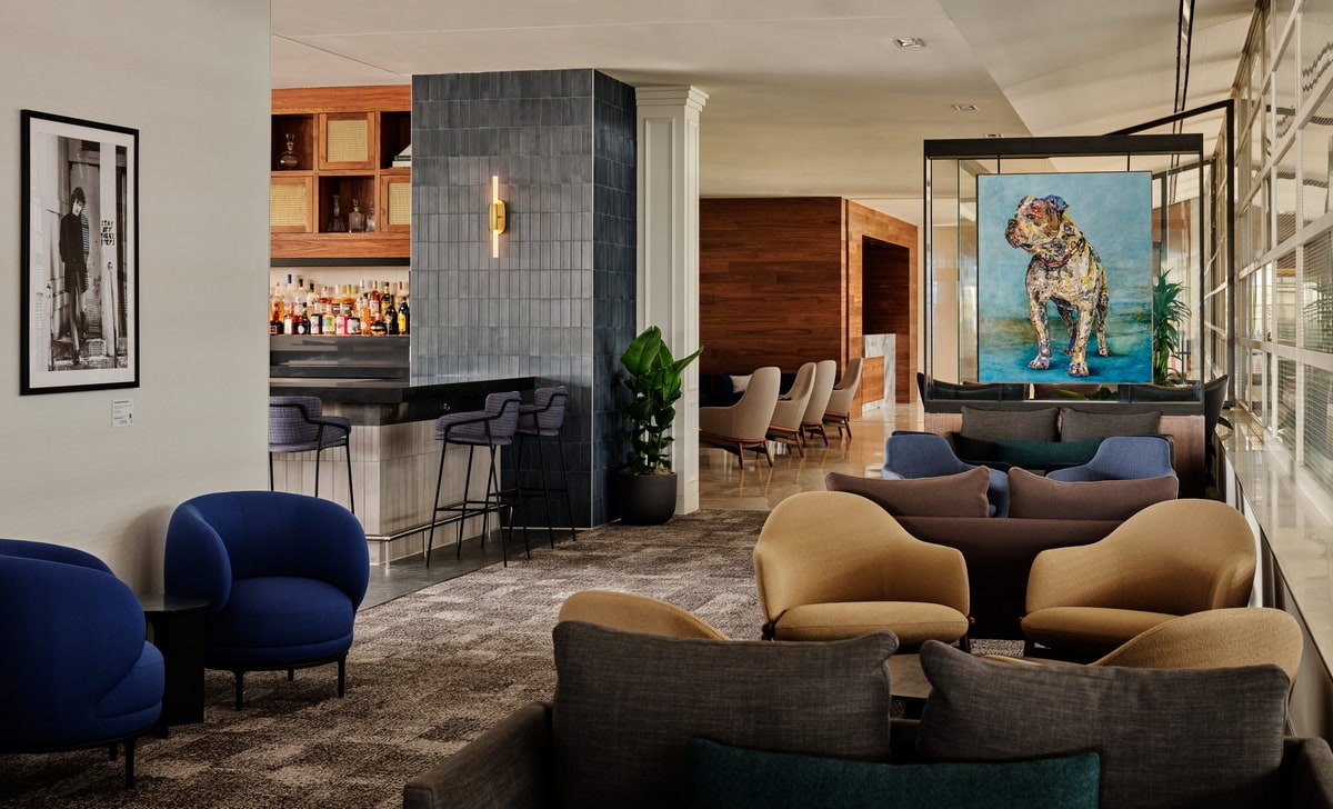 Lounge with art on the walls and seating, with the bar in the background.