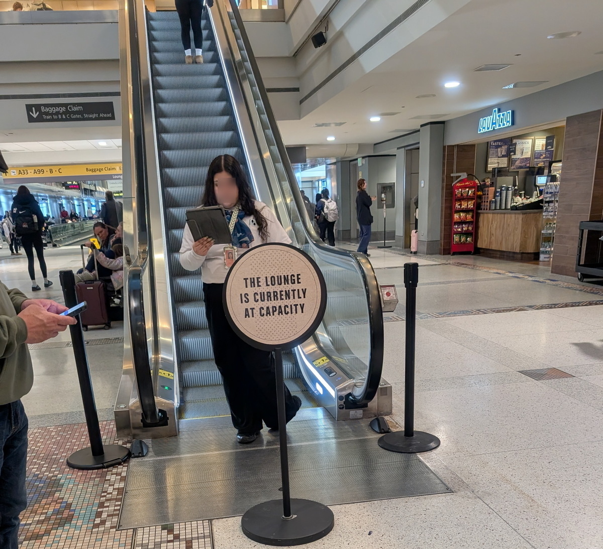 Sign at the entrance to a Capital One lounge escalator, saying The Lounge is Currently at Capacity