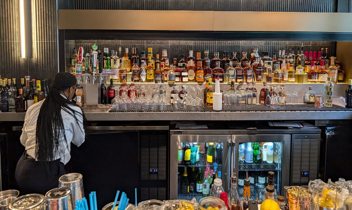 bar with bottles on the back wall, and a person working, preparing drinks.