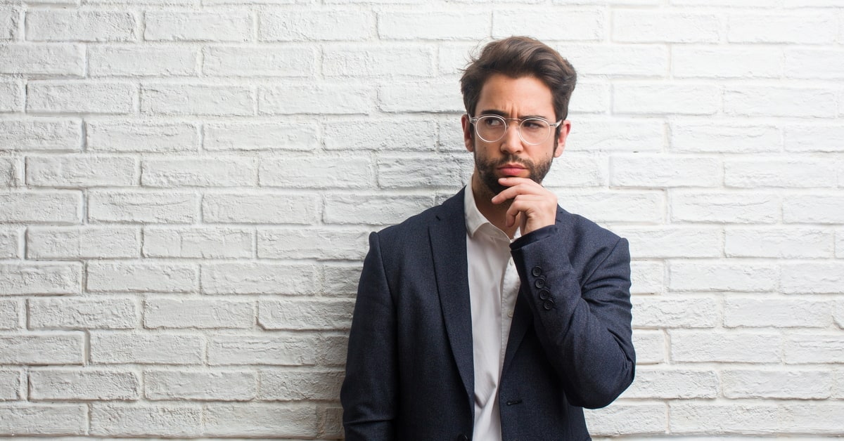 man wearing a sports coat leaning against wall looking disappointed.