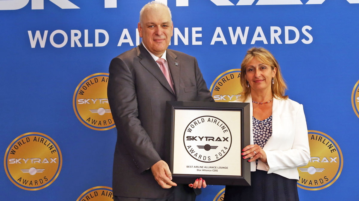 Two people standing on stage holding the award for the Best Alliance Lounge 2024.