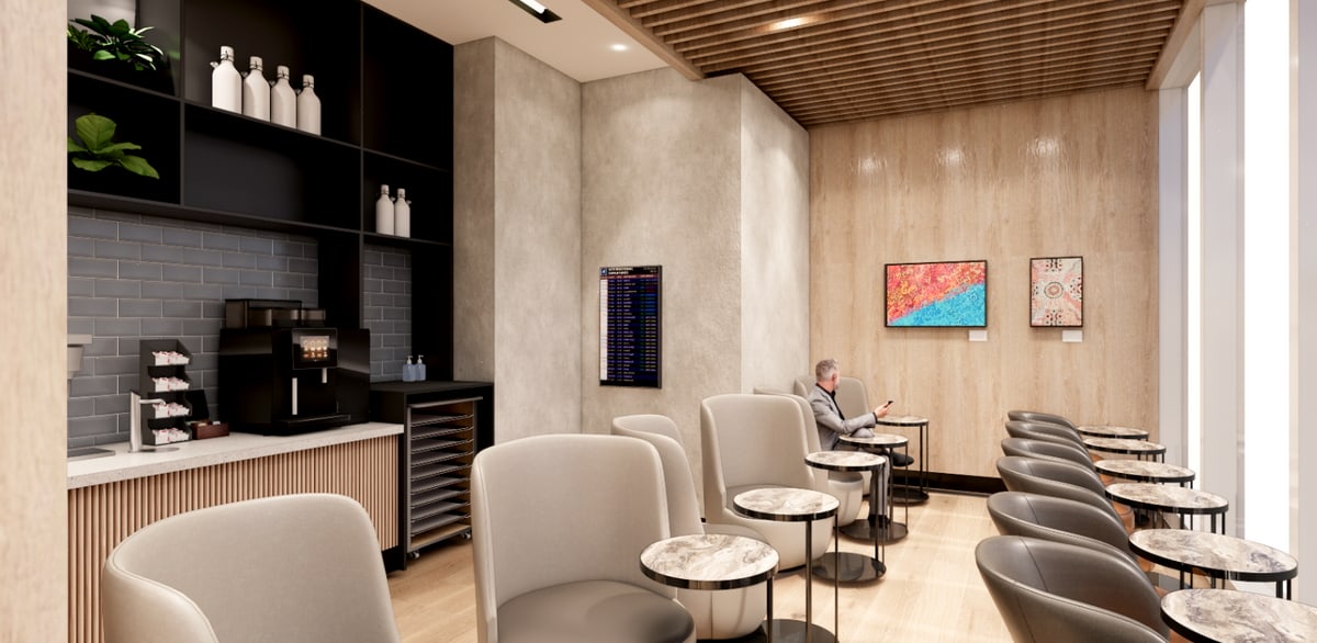 Seating area with a person sitting at a small table with flight monitor on the wall.