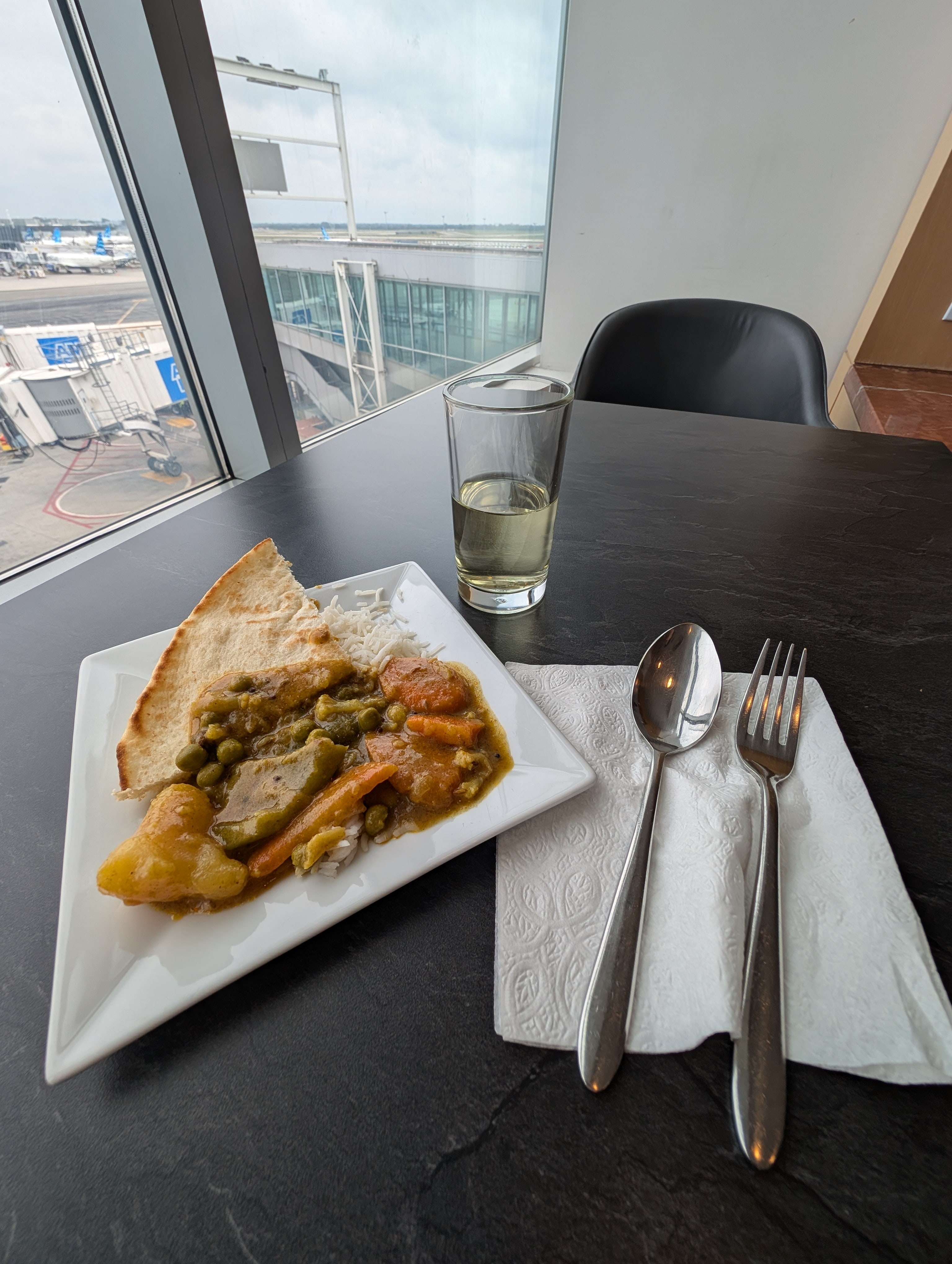 curry vegetables, nann, and white wine on table with view outdoors.