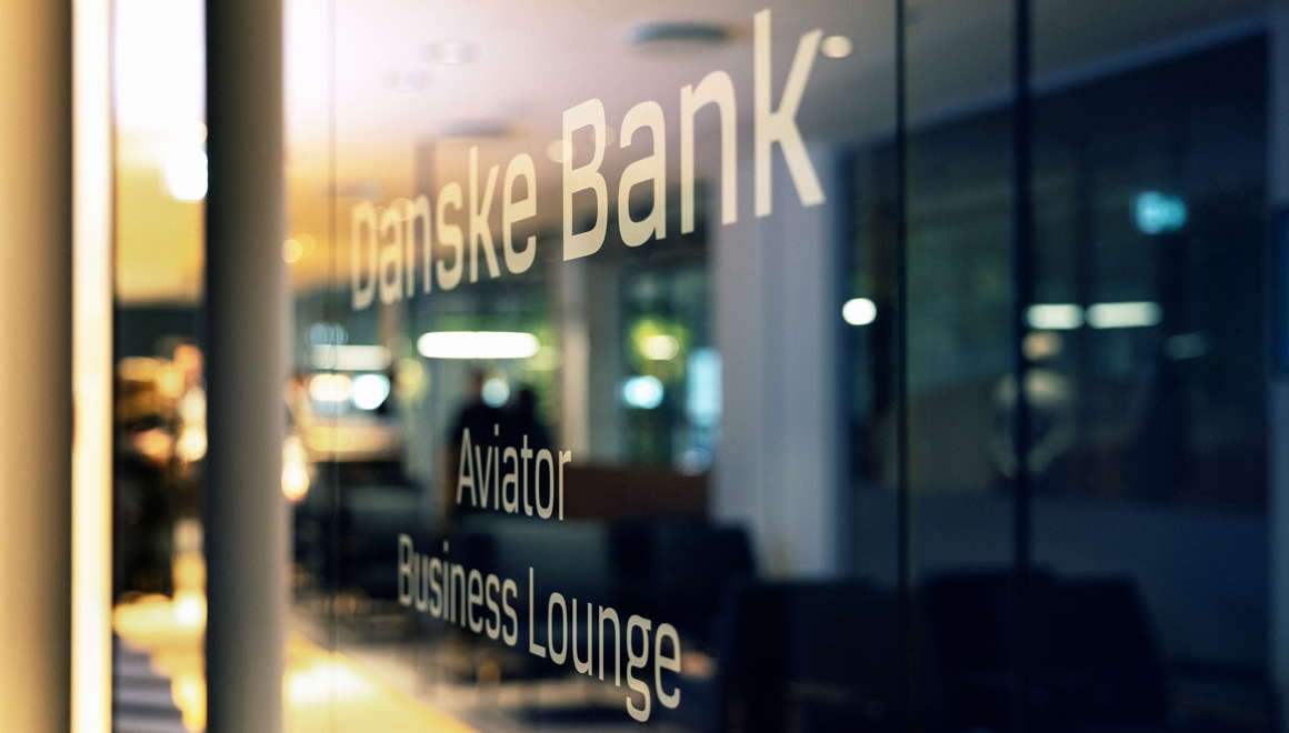 The glass door entrance to the lounge showing Danske Bank Aviator Business Lounge printed in gold writing on glass.