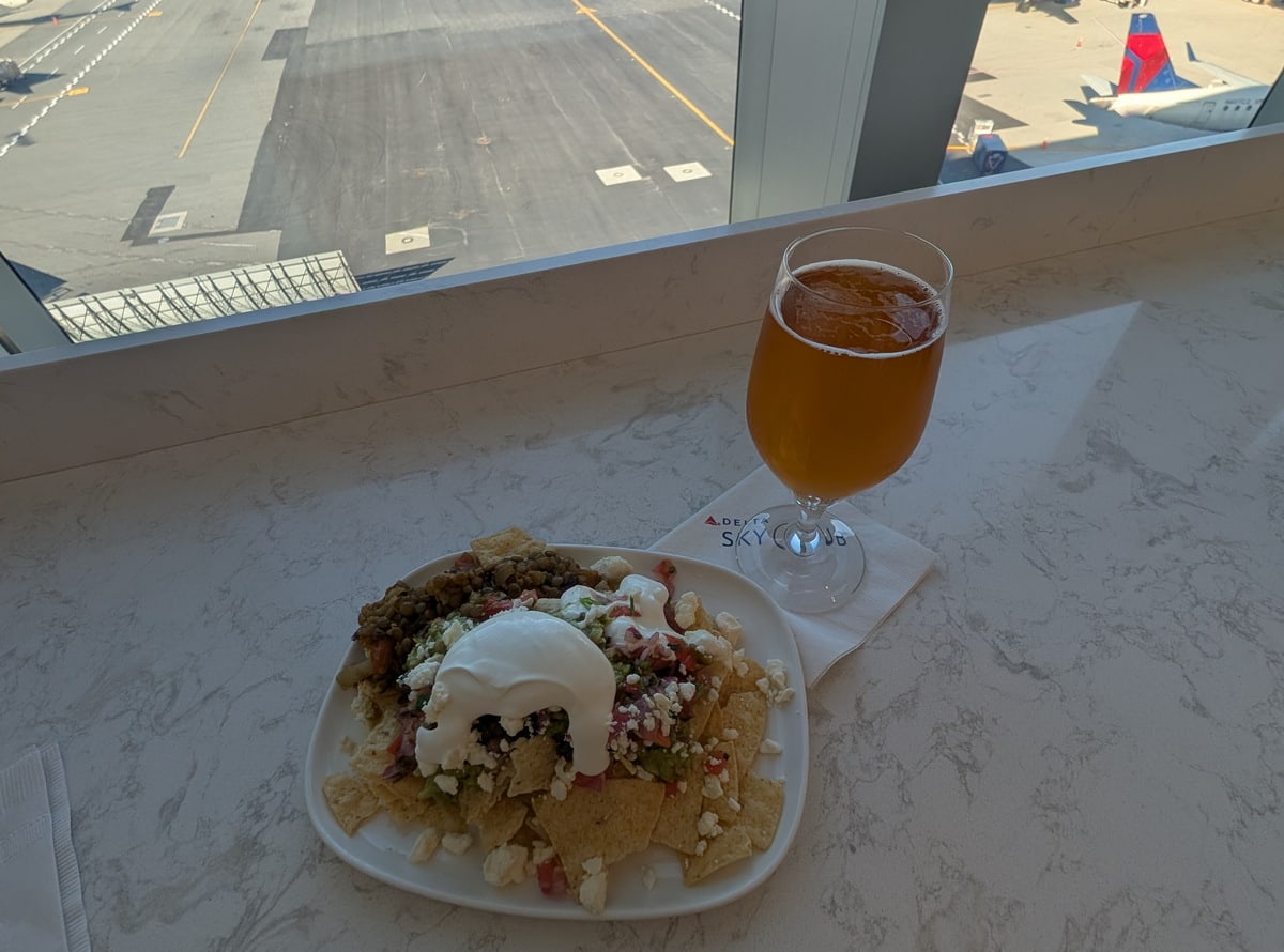 Nachos on a plate with a beer, sitting on a table with windows in the background.