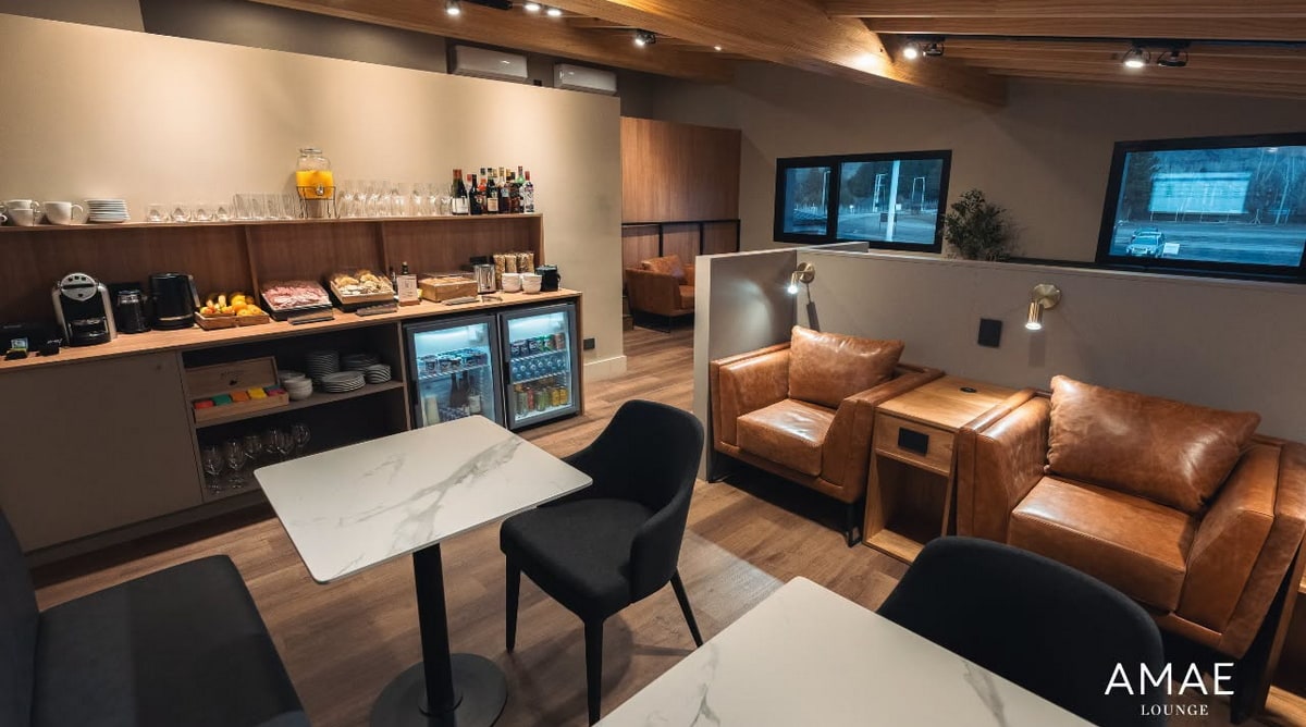 inside of the lounge showing tables, chairs, and windows in the background, with buffet and drinks.