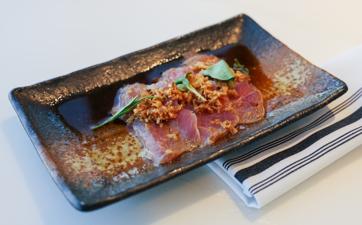 three pieces of Hamachi Crudo fish served on rustic plate, with a cloth napkin under the plate.