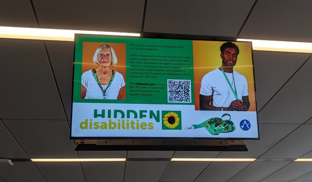 digital sign hanging at an airport, with a message about the Hidden Disabilities Sunflower program and how to learn more.