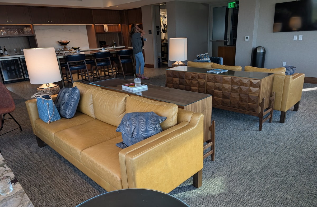 view inside the lounge showing sofas, seating, TVs, and food area in the background.