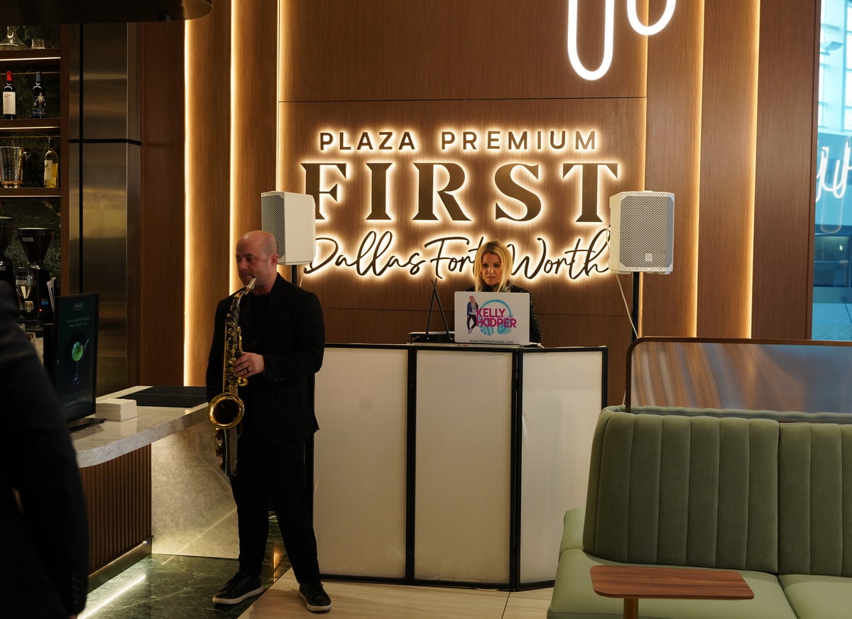 Saxophone player and DJ with a laptop, with lighted Plaza Premium First sign behind them.
