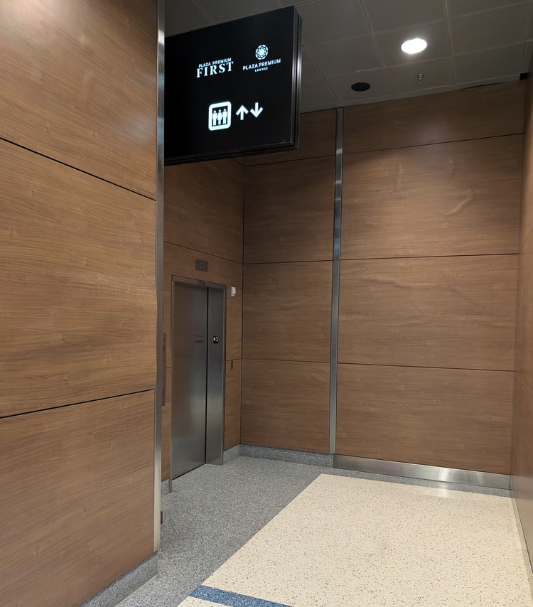 elevator inside of small enclosed area, with sign showing Plaza Premium Lounge.