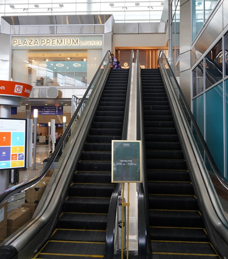 two escalators leading up to the lounge area, with the a sign reading Plaza Premium Lounge at the top.