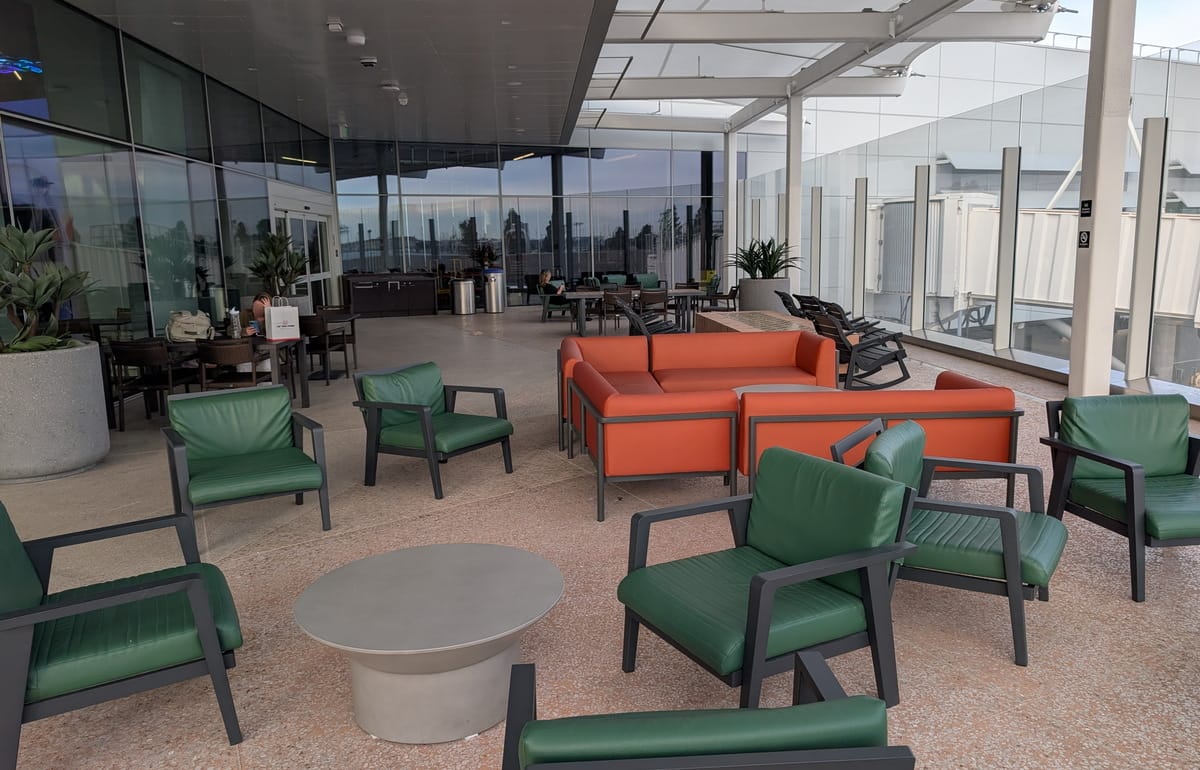 outdoor patio showing tables, chairs, and sofa, with recycling and trash in the background.