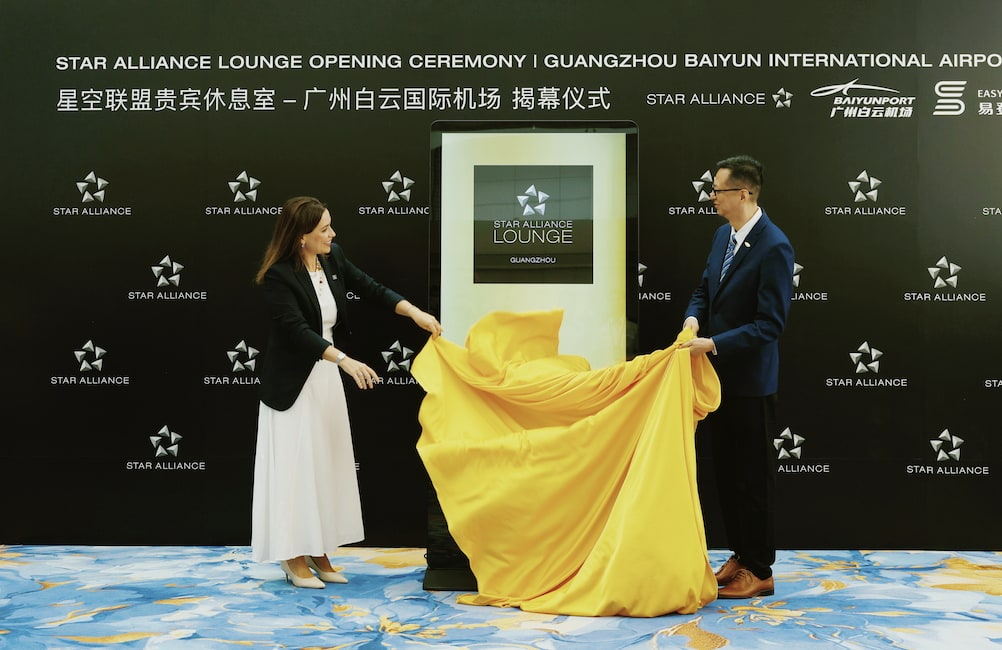 Two people standing in front of a Star Alliance sign pulling off a cover during the grand opening.