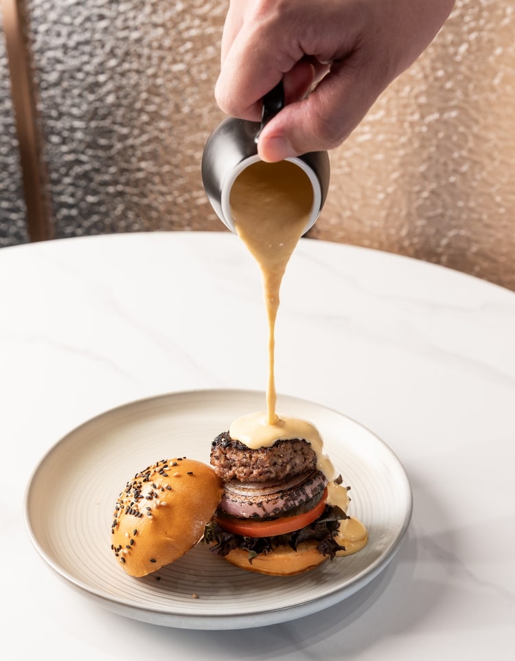 mini tavern burger on a plate with a chef pouring cheese on top.