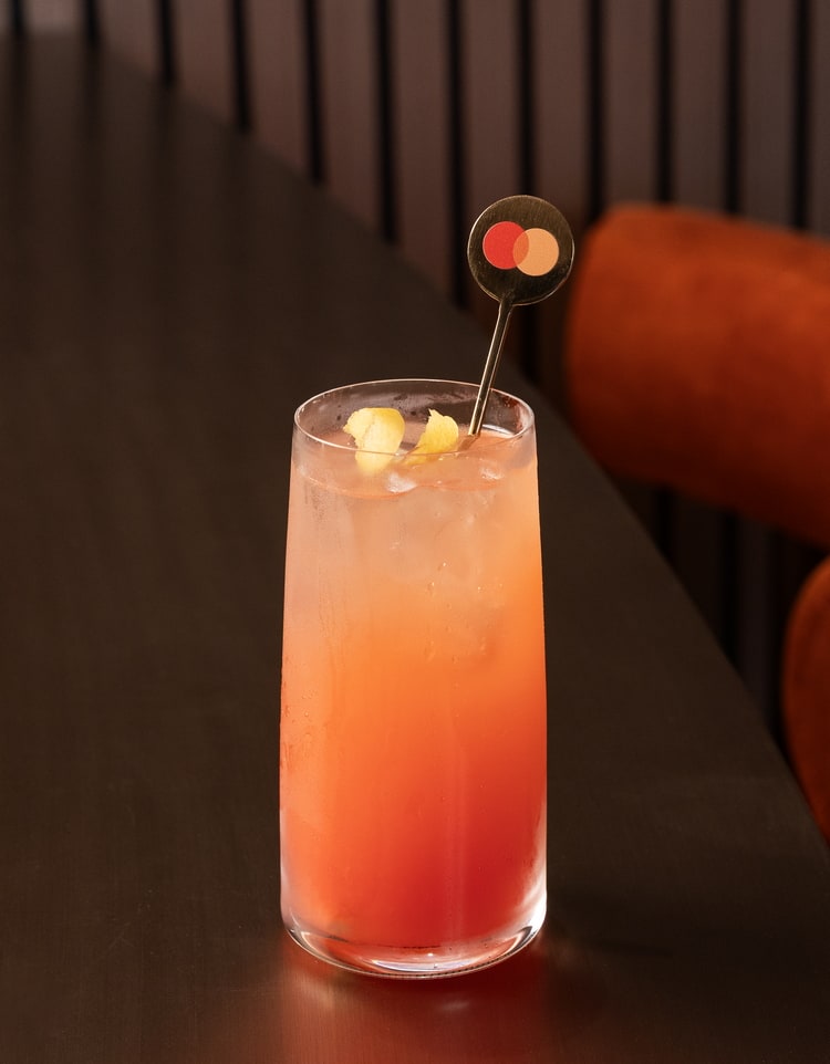Victoria Sunset cocktail sitting on a table with a Mastercard drink stir.
