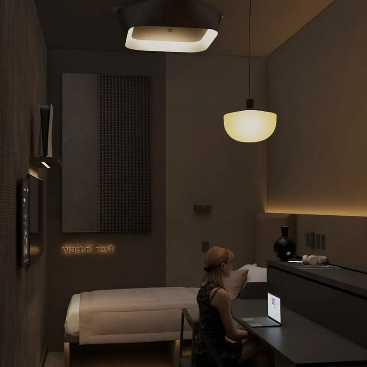 wait n' rest room rendering with person sitting at desk and bed in the background.